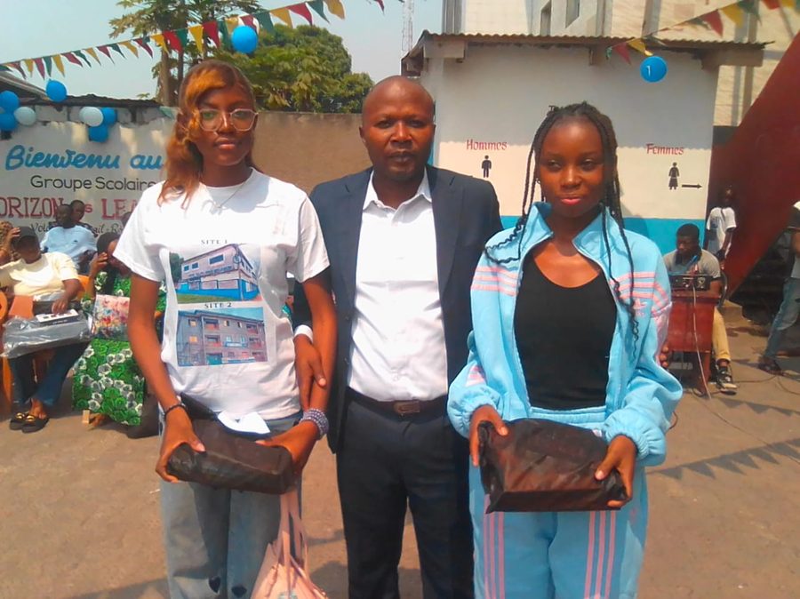 Deux élèves posant avec un adulte lors d'une cérémonie à l'école